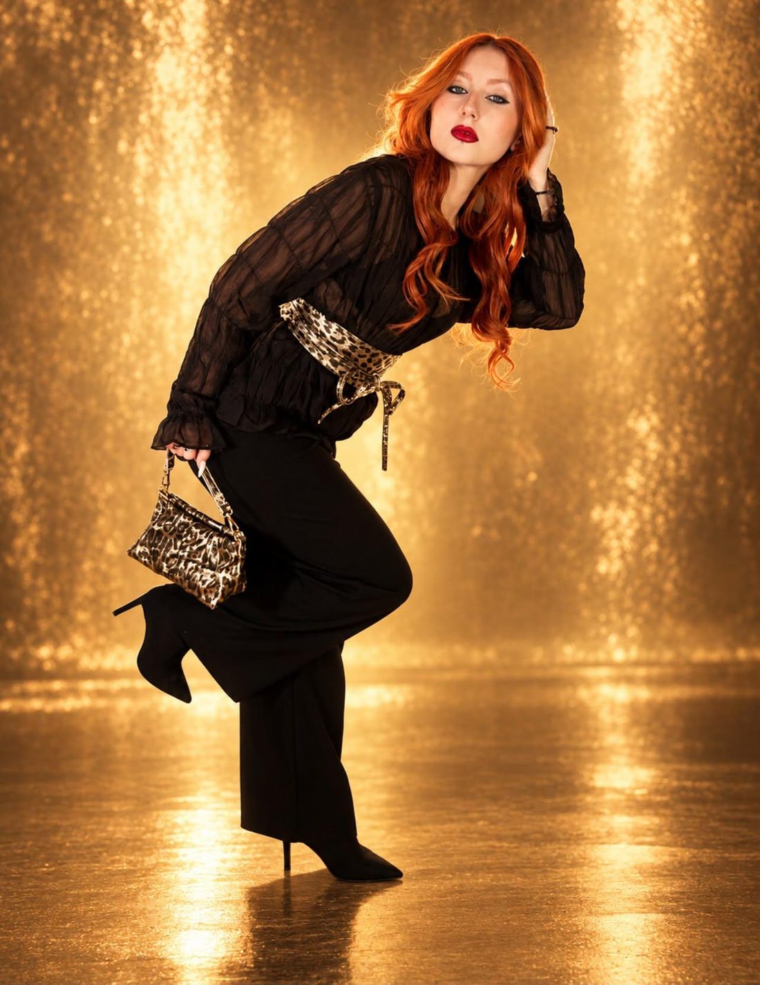 Alma, de pelo naranja y vestida de negro, posando ante un fondo dorado con destellos